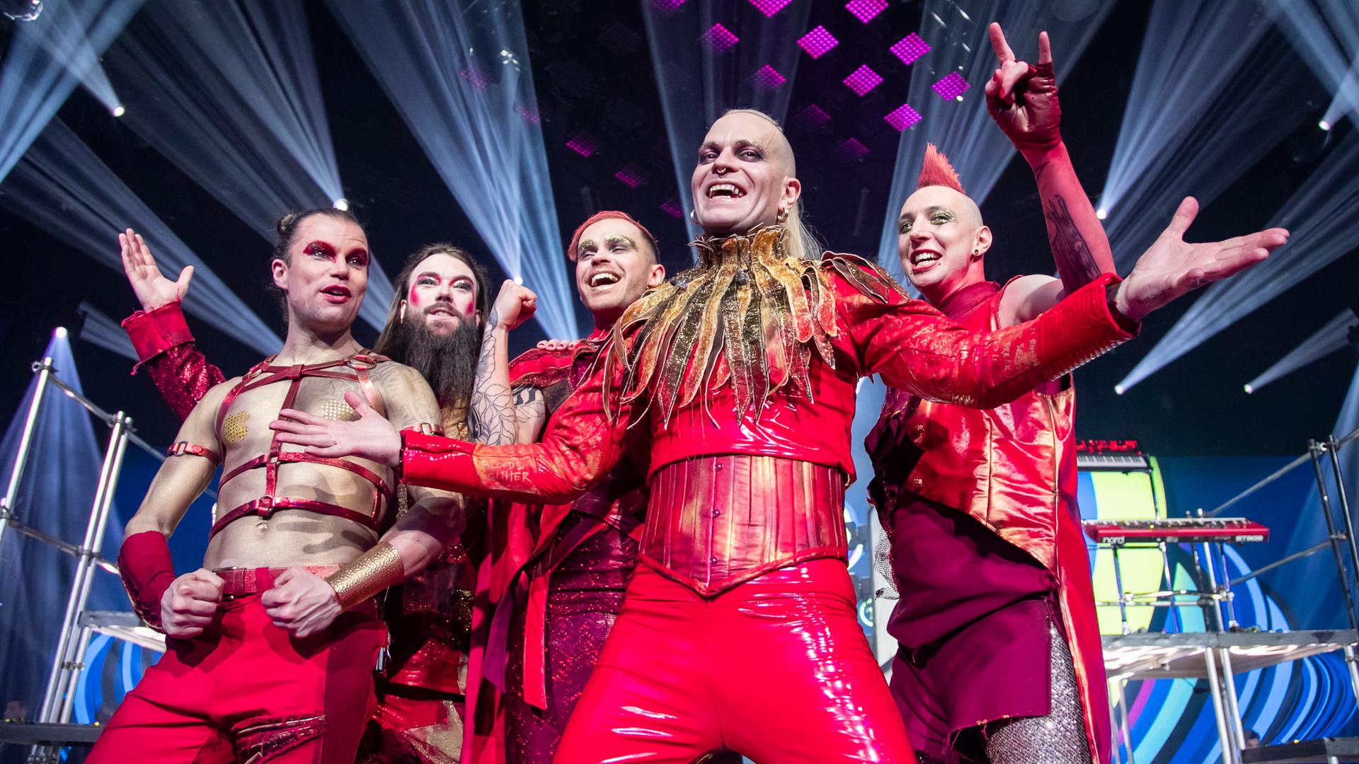 Die Band Lord Of The Lost posiert in roten Kostümen auf der Bühne und guckt in die Kamera.