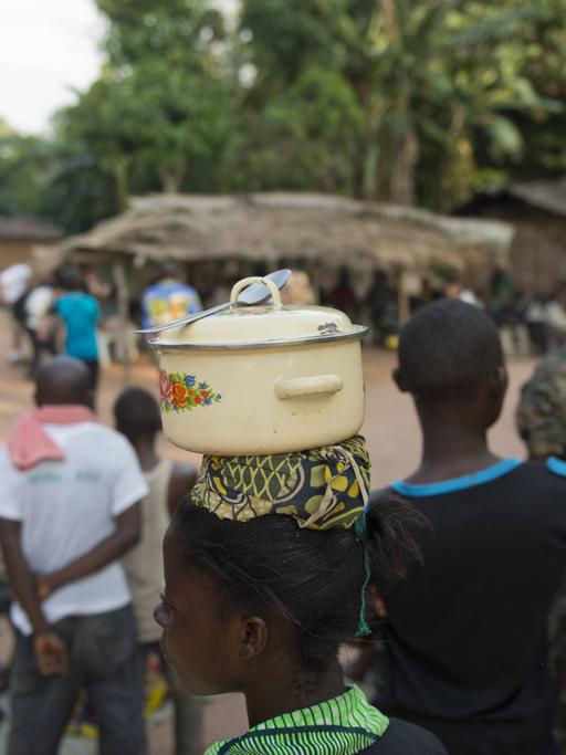 Eine junge Frau des indigenen Volks der BaAka (Pygmäen) trägt einen Kochtopf mit Löffel auf dem Kopf, in ihrem Dorf bei Bayanga im Dzanga-Nationalpark 
