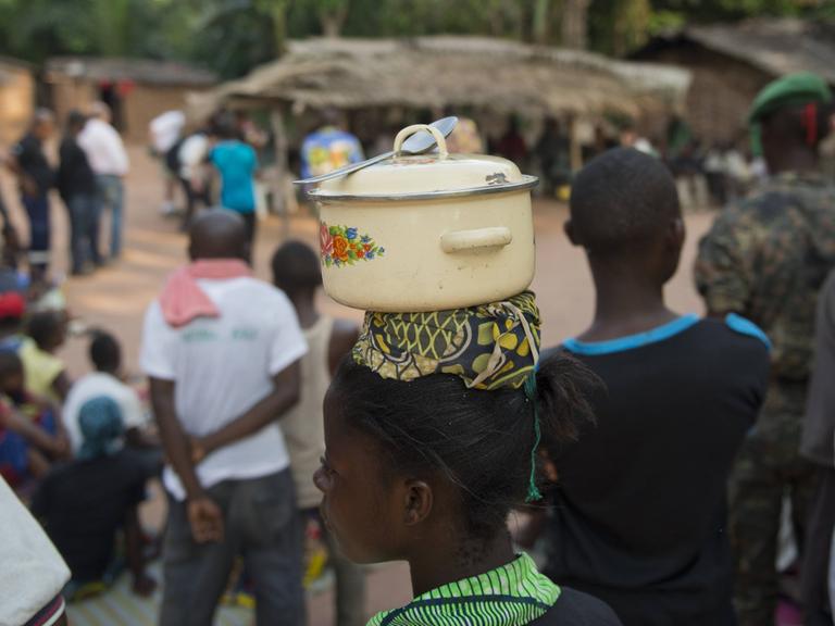 Eine junge Frau des indigenen Volks der BaAka (Pygmäen) trägt einen Kochtopf mit Löffel auf dem Kopf, in ihrem Dorf bei Bayanga im Dzanga-Nationalpark 