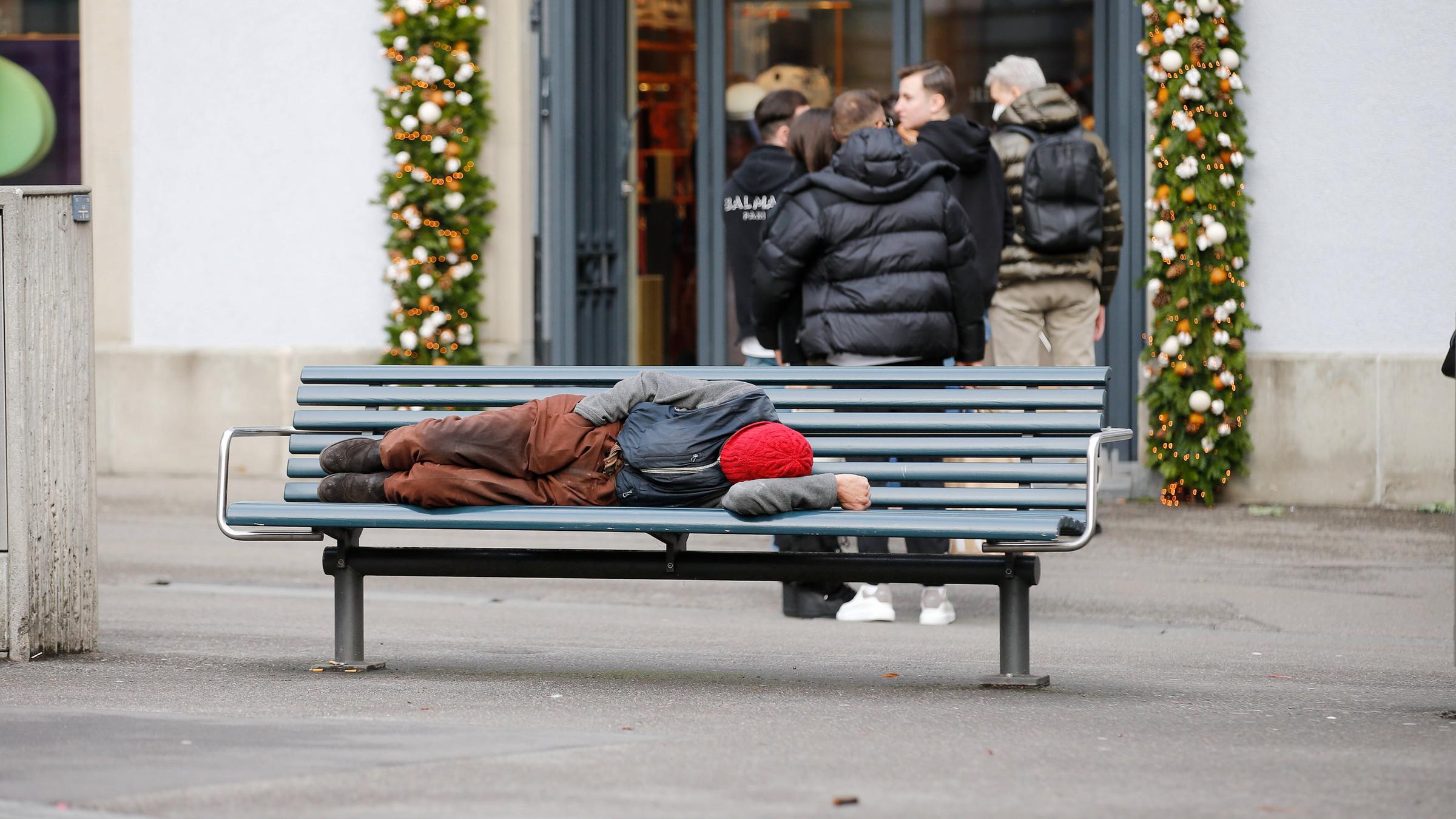 Foto Manuel Geisser 30.12.2021 Zürich : Armut . Mann auf einer Parkbank . Hinten stehen Passanten Schlange vor einem Kle Foto Manuel Geisser 30.12.2021 Zürich : Armut . Mann auf einer Parkbank . Hinten stehen Passanten Schlange vor einem Kle