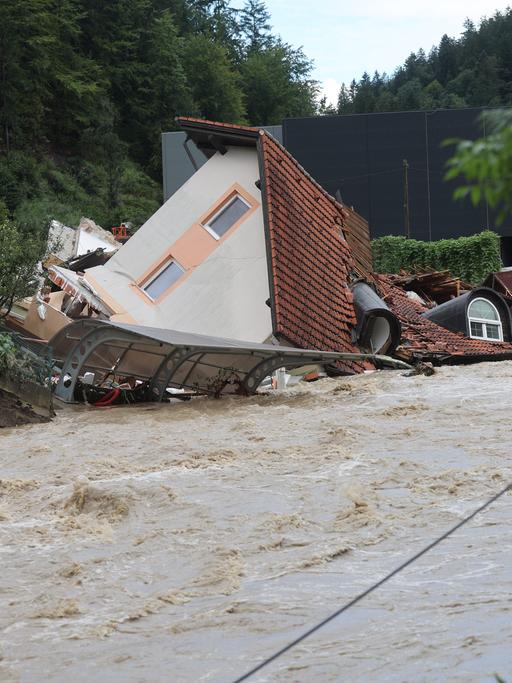 Ein zerstörtes Haus, auf dem Dach liegend inmitten eines reißenden Stroms. 