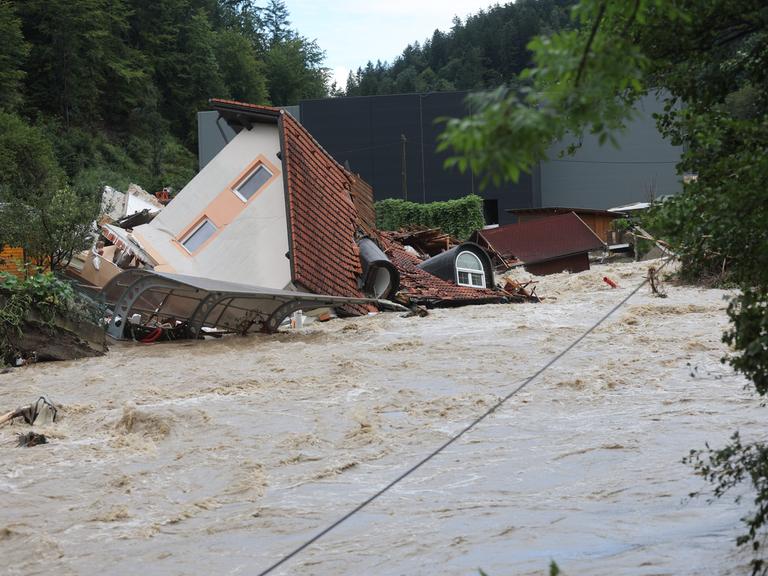 Ein zerstörtes Haus, auf dem Dach liegend inmitten eines reißenden Stroms. 