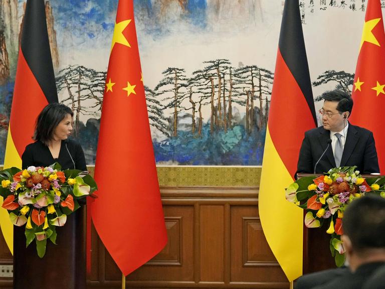 Annalena Baerbock, und Qin Gang R sprechen auf einer Pressekonferenz. Sie stehen an zwei Rednerpulten, hinter ihnen jeweils die Flaggen der beiden Länder.