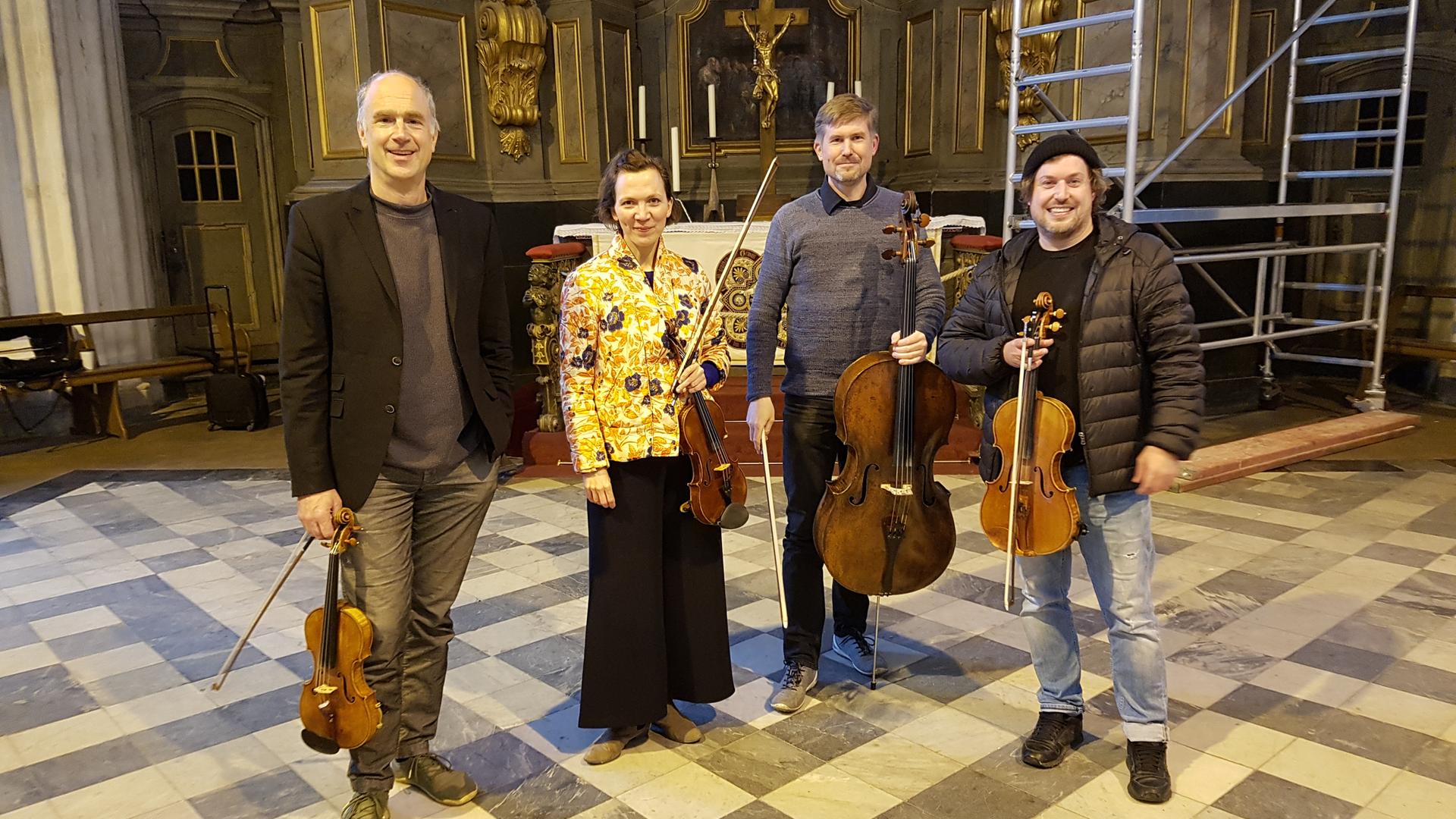 Drei Musiker und eine Musikerin stehen mit ihren Instrumenten (Violinen und ein Kontrabass) in der Rostocker Marienkirche