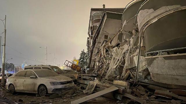 Türkei, Diyarbakir: Beschädigte Fahrzeuge parken vor einem eingestürzten Gebäude nach einem Erdbeben.