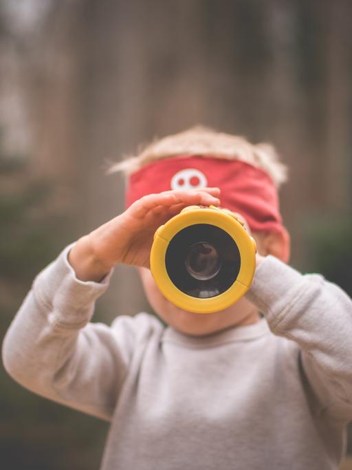 Ein Kind mit einer Piratenmütze auf dem Kopf schaut durch ein gelbes Fernrohr. Das Gesicht bleibt dahinter verborgen. Der Bildfokus liegt vorn auf dem Fernrohr.