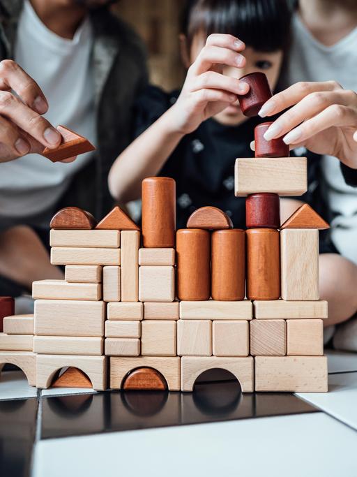 Eine Familie mit Kind baut ein komplexes Gebilde aus Holzbausteinen.