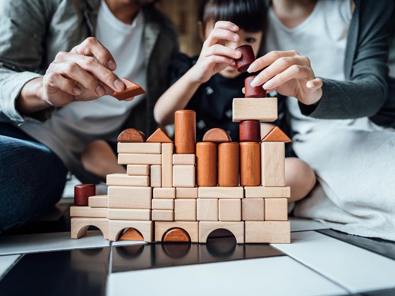 Eine Familie mit Kind baut ein komplexes Gebilde aus Holzbausteinen.