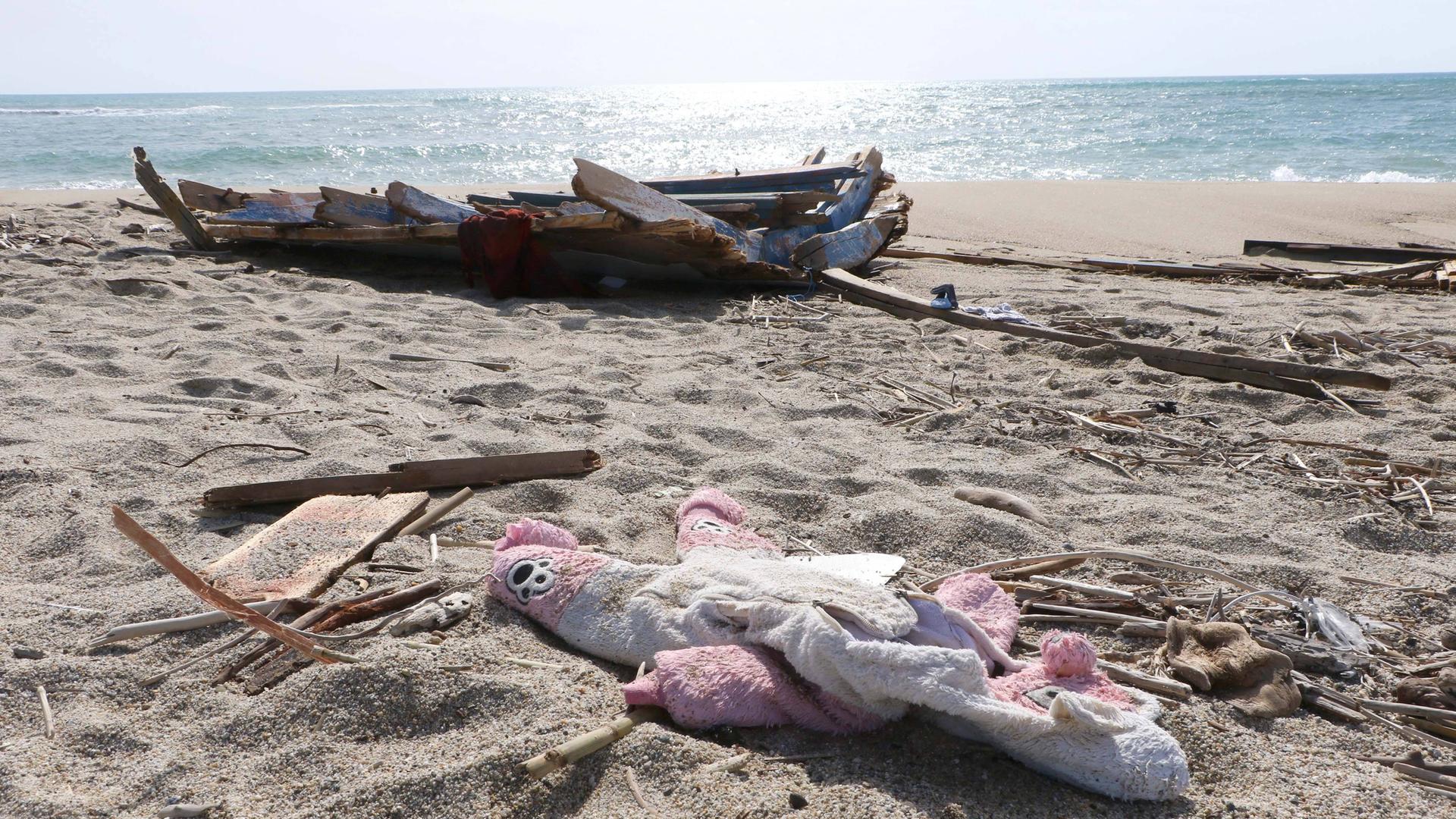 Trümmer von dem Boot und ein Kuschel-Tier liegen an einem Strand. Trümmer von dem Boot und ein Kuschel-Tier liegen an einem Strand.