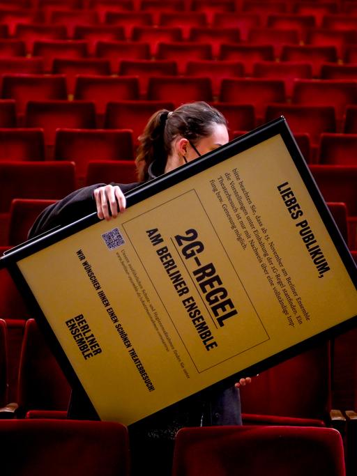 Eine Mitarbeiterin trägt einen Aufsteller mit dem Hinweis auf die 2G-Regel durch den Zuschauerraum des Berliner Ensemble.