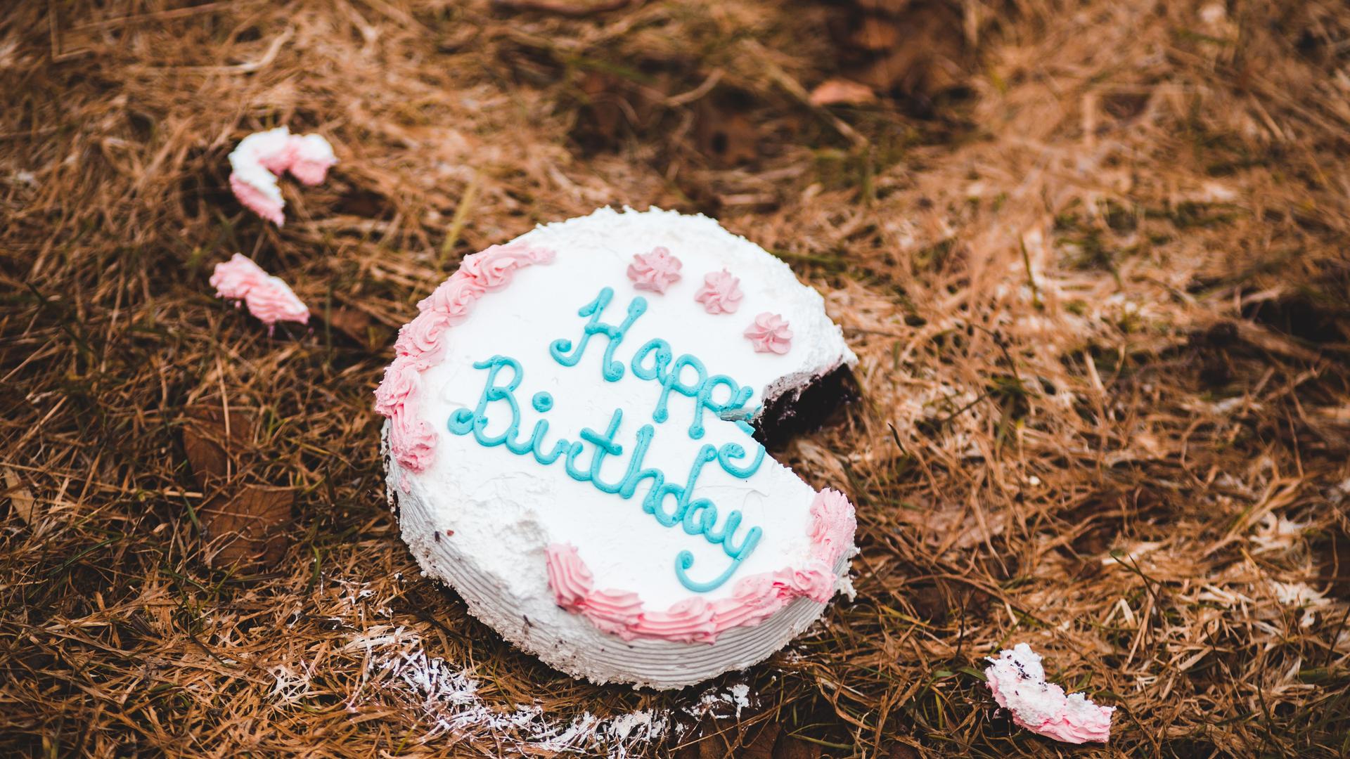 Eine Torte mit der Aufschrift Happy Birthday liegt auf dem Boden. Ein Stück fehlt und liegt in kleinen Teilen verstreut daneben. Eine Torte mit der Aufschrift Happy Birthday liegt auf dem Boden. Ein Stück fehlt und liegt in kleinen Teilen verstreut daneben.