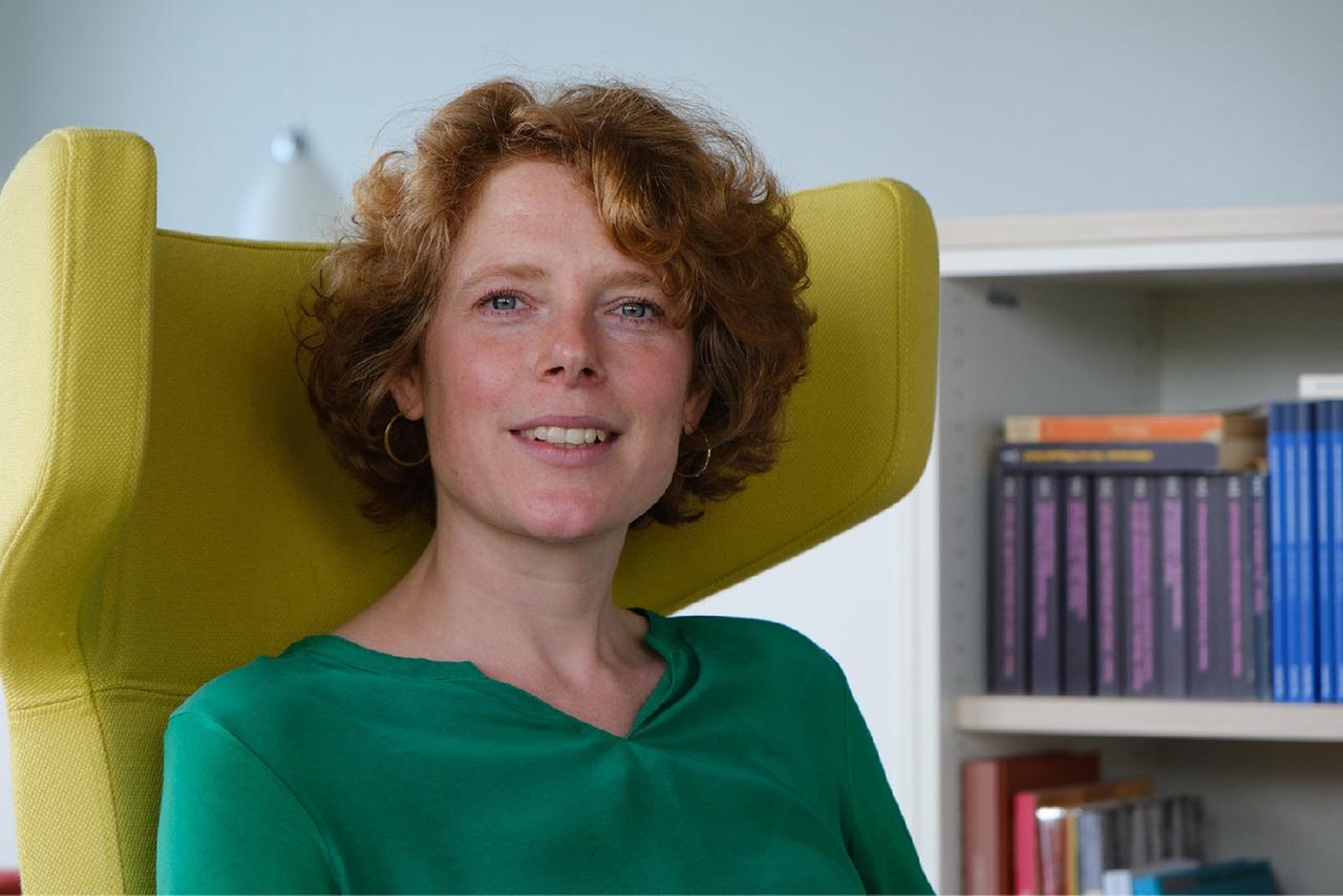 Die Religionssoziologin Maren Freudenberg trägt eine grüne Bluse und sitzt in einem gelben Lehnstuhl.