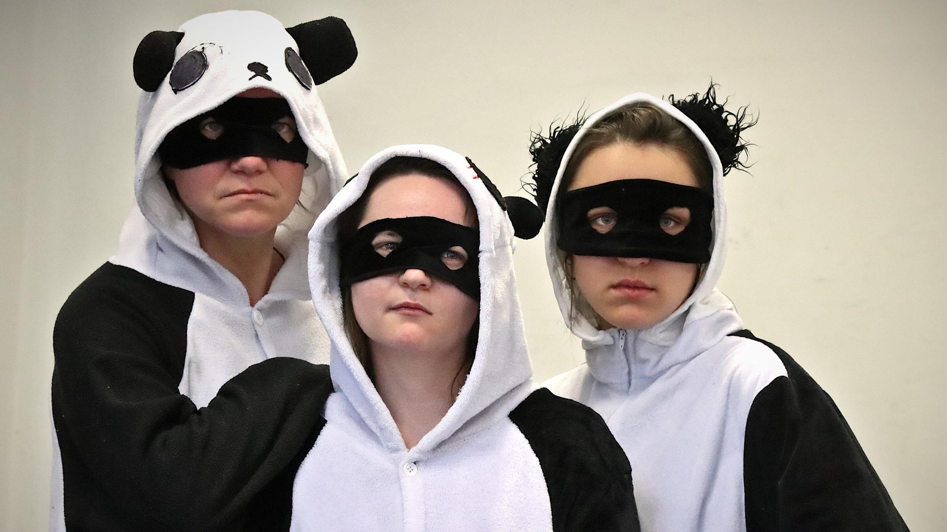 Drei Frauen in Panda-Kostümen schauen ernst in die Kamera.