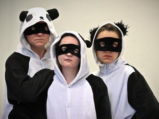 Drei Frauen in Panda-Kostümen schauen ernst in die Kamera.