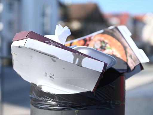 Pizzakartons und andere Essensverpackungen stecken in einem öffentlichen Mülleimer