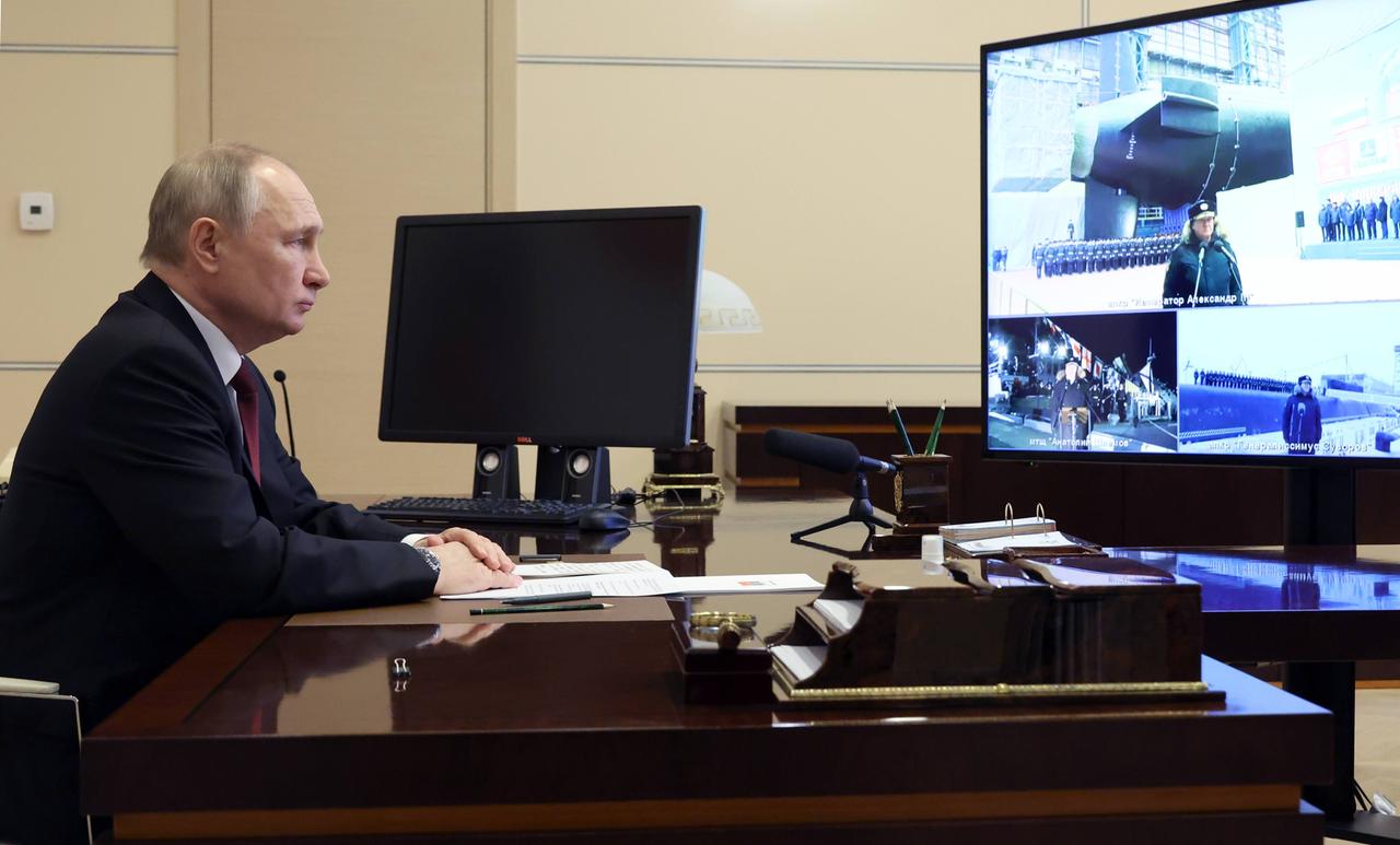 Russlands Präsident Putin sitzt an einem Schreibtisch und schaut auf einen Bildschirm. Darauf sind Kriegsschiffe und Soldaten zu sehen. 