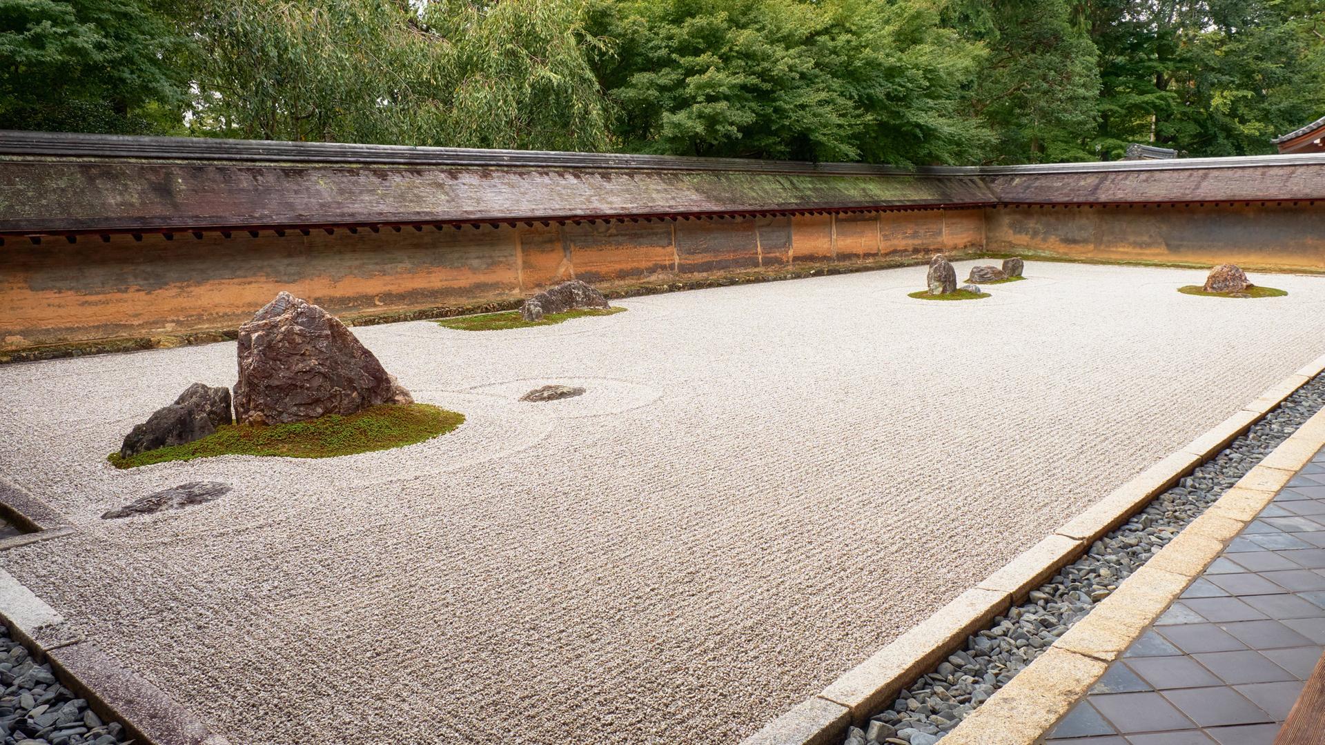 Ein Rechteck auf dem Boden, gefüllt mit fein säuberlich geharktem Sand. Im Sand sind Steine ​​angeordnet. Es handelt sich um einen Steingarten im Ryōan-ji-Tempel in Kyoto.