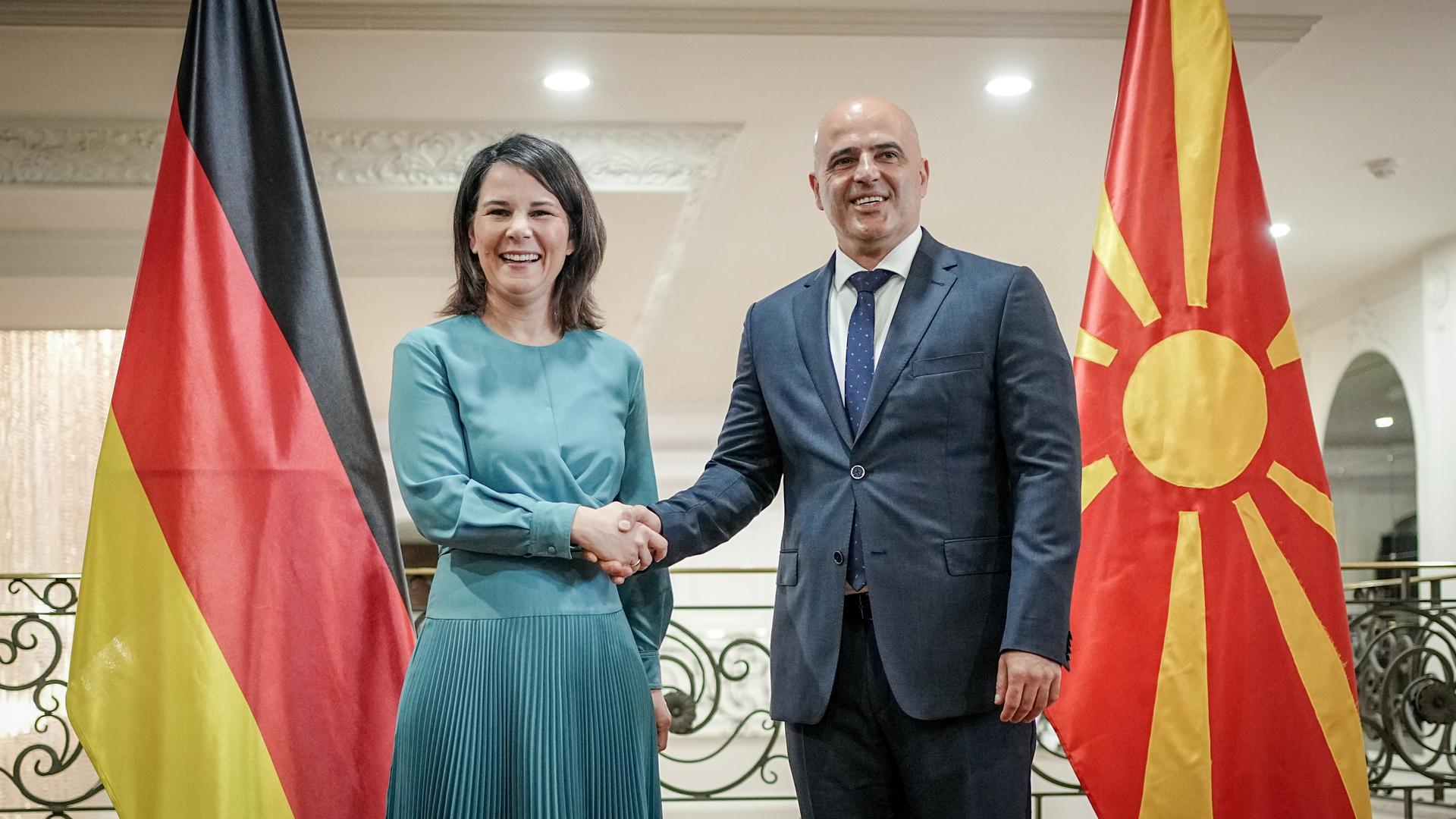 Annalena Baerbock und Dimitar Kovahevski geben sich die Hand. Beide lachen. Neben den Politikern steht jeweils die deutsche und die nordmazedonische Flagge. Annalena Baerbock und Dimitar Kovahevski geben sich die Hand. Beide lachen. Neben den Politikern steht jeweils die deutsche und die nordmazedonische Flagge.