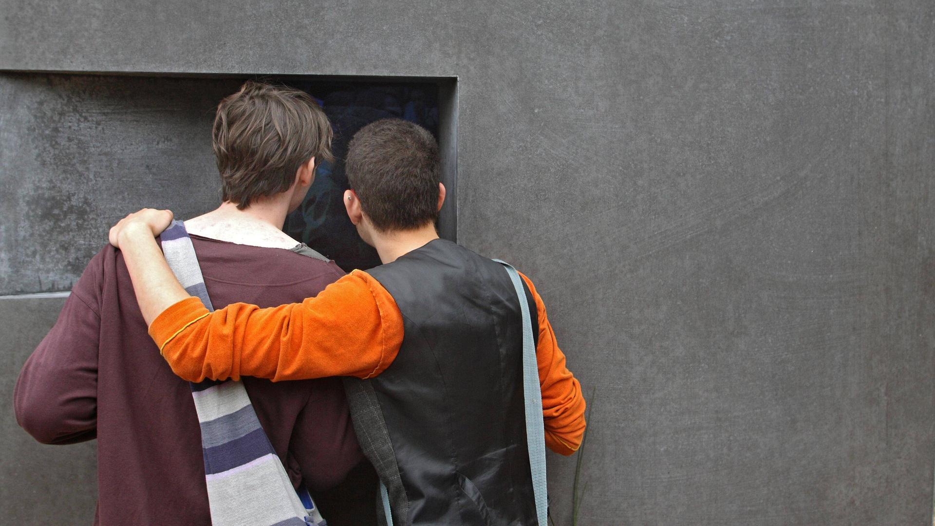 Zwei Männer stehen Arm in Arm vor dem Denkmal für die im Nationalsozialismus verfolgten Homosexuellen in Berlin.  
