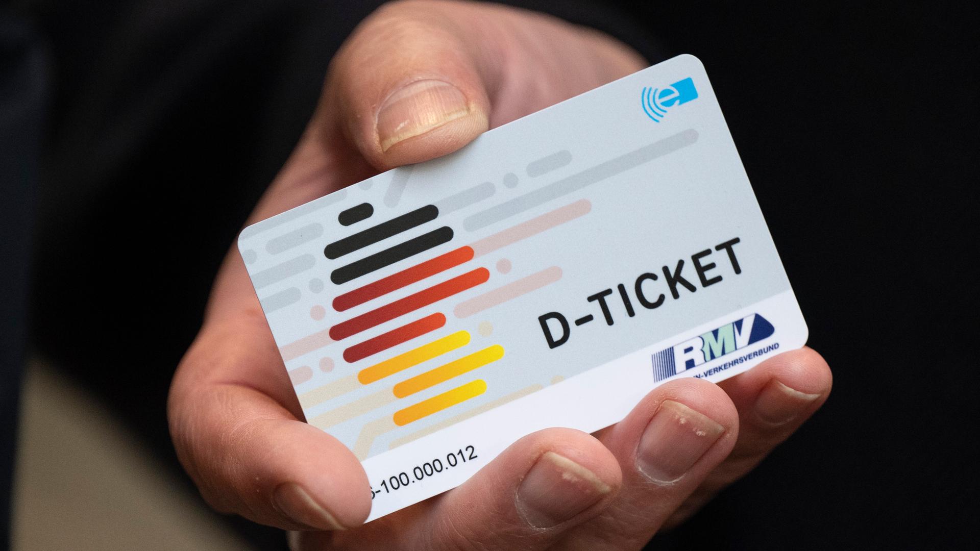 Eine Hand hält eine Plastik-Karte in die Kamera. Darauf steht "D-Ticket". Und man sieht eine Karte von Deutschland. Die Karte hat die Farben schwarz-rot-gelb. Eine Hand hält eine Plastik-Karte in die Kamera. Darauf steht "D-Ticket". Und man sieht eine Karte von Deutschland. Die Karte hat die Farben schwarz-rot-gelb.