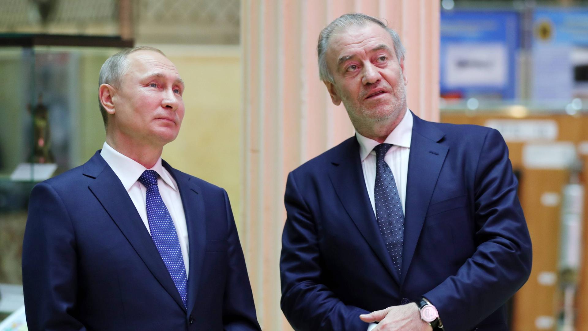 Der russische Präsident Wladimir Putin und der Dirigent Waleri Gergijew stehen nebeneinander. Putin auf der linken Seite, Gergijew auf der rechten. Sie tragen beide dunkelblaue Anzüge. Der russische Präsident Wladimir Putin und der Dirigent Waleri Gergijew stehen nebeneinander. Putin auf der linken Seite, Gergijew auf der rechten. Sie tragen beide dunkelblaue Anzüge.