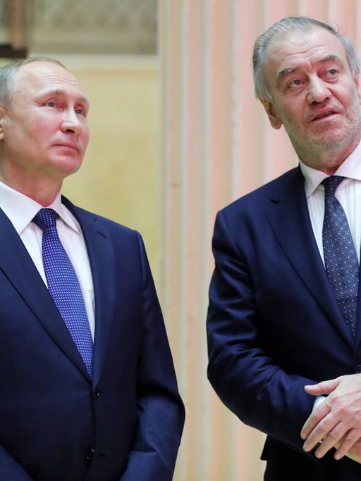 Der russische Präsident Wladimir Putin und der Dirigent Waleri Gergijew stehen nebeneinander. Putin auf der linken Seite, Gergijew auf der rechten. Sie tragen beide dunkelblaue Anzüge.