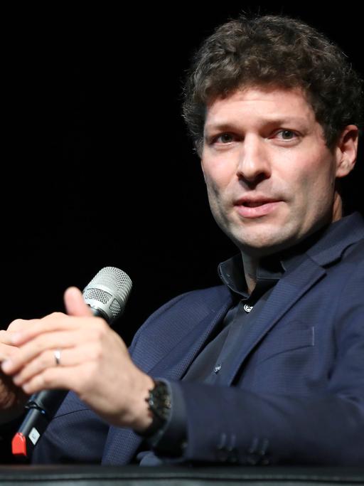Ronen Steinke spricht auf einem Podium in ein Mikrofon.