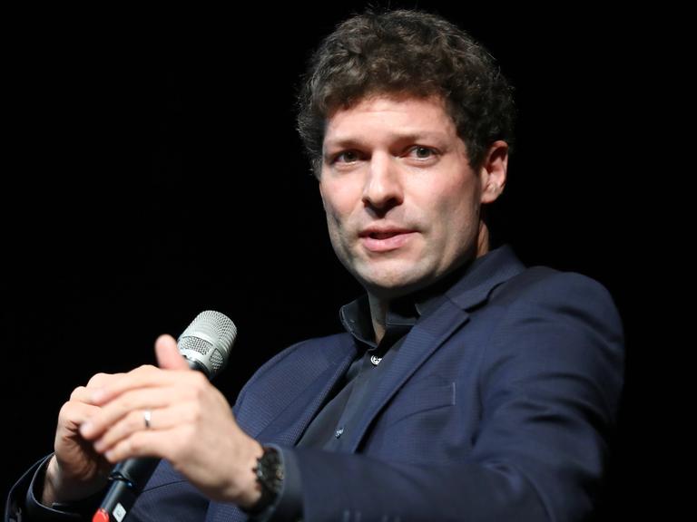 Ronen Steinke spricht auf einem Podium in ein Mikrofon.