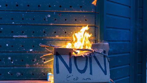 Ein Pappschild mit der französischen Aufschrift "Non" brennt vor einem geschlossenen Kiosk in Paris.