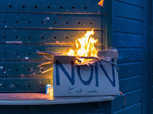 Ein Pappschild mit der französischen Aufschrift "Non" brennt vor einem geschlossenen Kiosk in Paris.