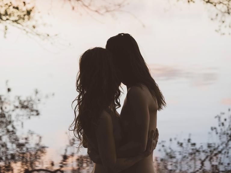 Die Silhouette eines Frauenpaares die sich umarmen, in romantischer Lichtstimmung vor einem See in Brandenburg.