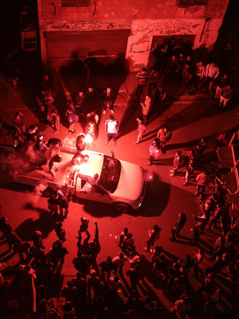 Luftaufnahme auf eine Ansammlung von Menschen bei Nacht von oben. In der Mitte ein Auto, darum sternenförmig tanzende Personen.