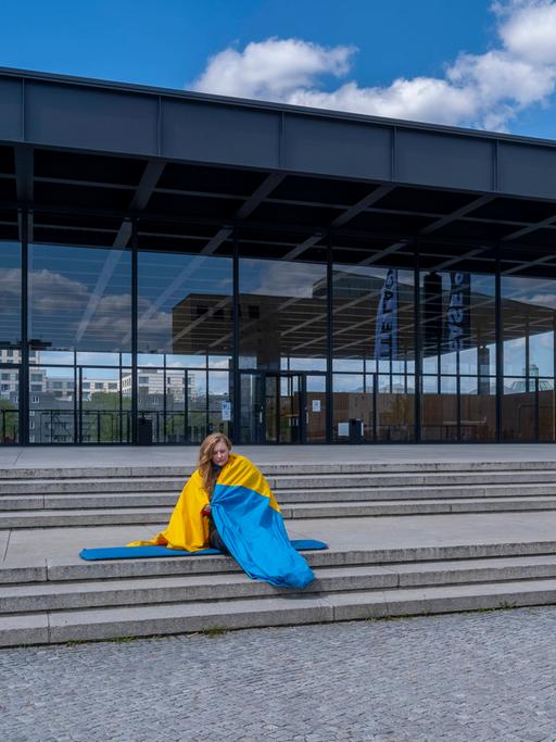 Eine Frau eingehüllt in die ukrainische Flagge vor der Neuen Nationalgalerie in Berlin.