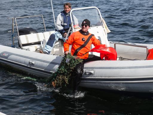 Ein Helfer holt alte Netze aus der Ostsee, die durch einen roten Hebesack an die Oberfläche befördert worden sind.