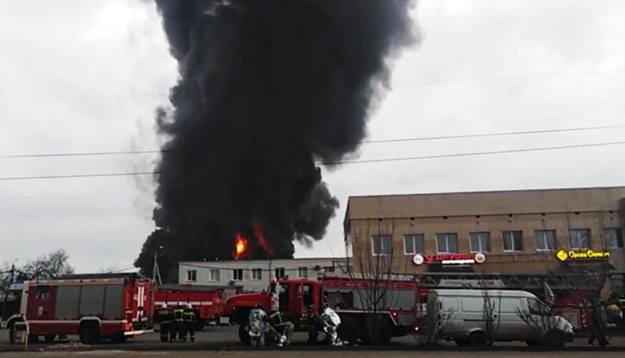 Feuerwehrwagen stehen auf einer Straße und löschen ein Feuer, aus dem eine riesige schwarze Rauchwolke hochsteigt. Feuerwehrwagen stehen auf einer Straße und löschen ein Feuer, aus dem eine riesige schwarze Rauchwolke hochsteigt.