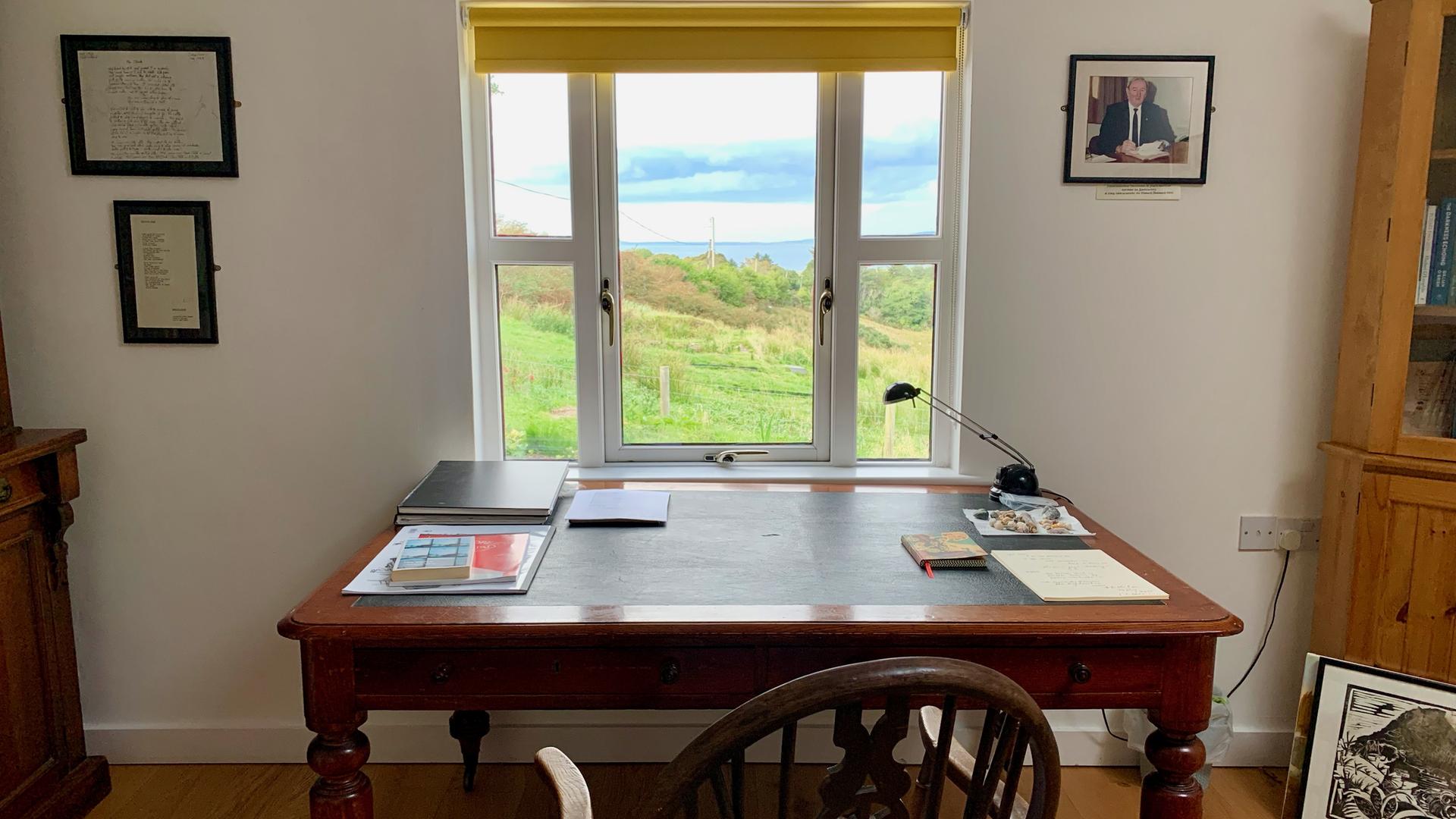 Ein Schreibtisch am Fenster mit Blick auf eine grüne Wiese und das Meer Ein Schreibtisch am Fenster mit Blick auf eine grüne Wiese und das Meer