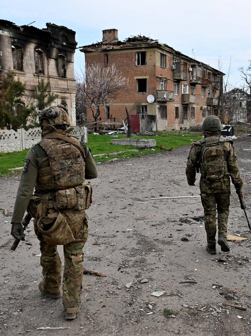 Drei bewaffnete Männer in Soldatenuniformen patrouillieren durch eine vom Krieg schwer beschädigte Kleinstadt.