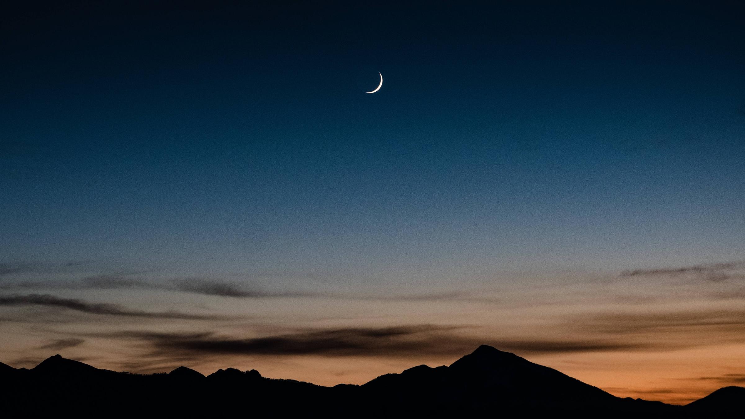 Eine Mondsichel erhellt die Landschaft in der Abenddämmerung