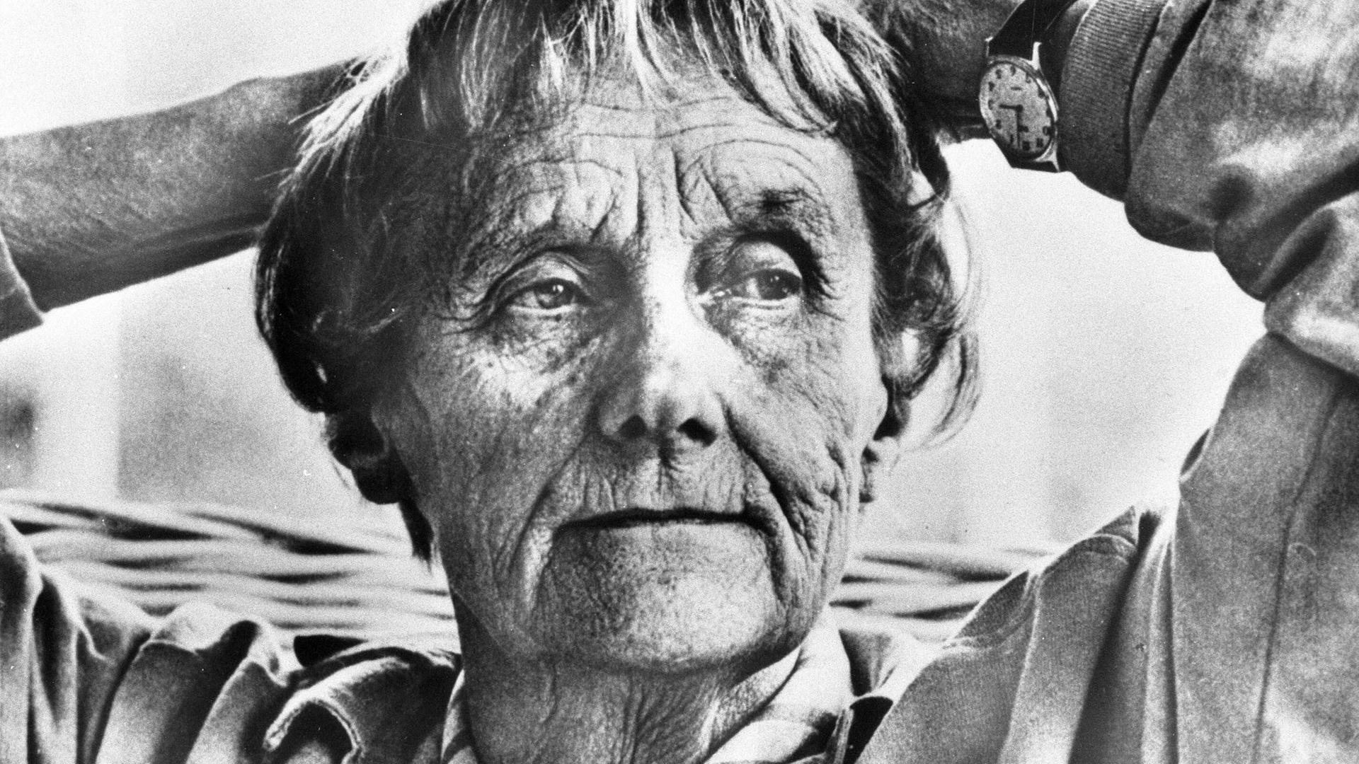 Das Schwarz-Weiß-Foto zeigt eine rund 80 Jahre alte Frau, die sich zurücklehnt und die Hände hinter dem Kopf verschränkt. Das Schwarz-Weiß-Foto zeigt eine rund 80 Jahre alte Frau, die sich zurücklehnt und die Hände hinter dem Kopf verschränkt.