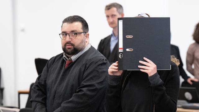 Auf dem Foto hält sich die Angeklagte Lina E. einen Akten-Ordner vor das Gesicht.