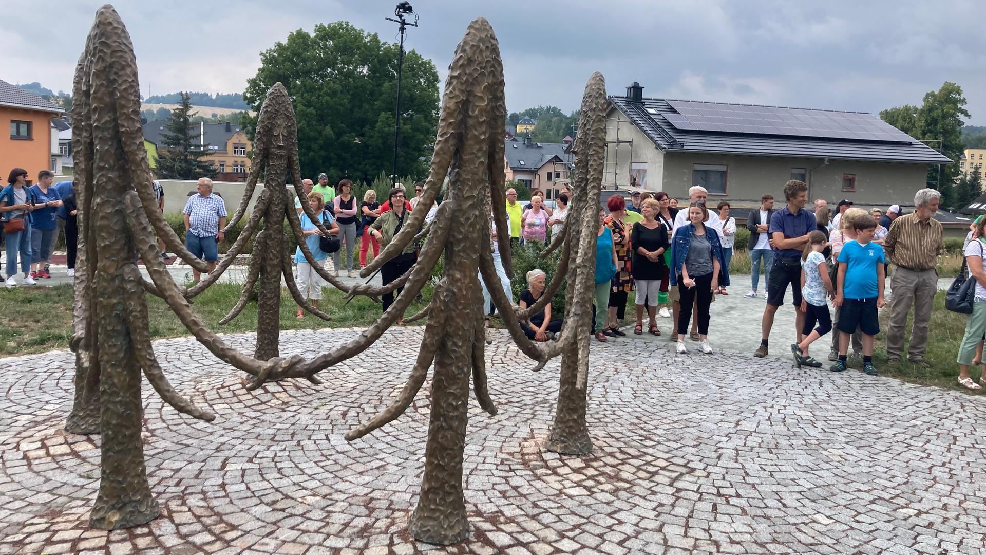 Sechs Fichten aus Bronze stehen in einem Kreis und halten sich freundschaftlich an den Ästen. Erst auf den zweiten Blick sieht man ihre Gesichter. Sechs Fichten aus Bronze stehen in einem Kreis und halten sich freundschaftlich an den Ästen. Erst auf den zweiten Blick sieht man ihre Gesichter.