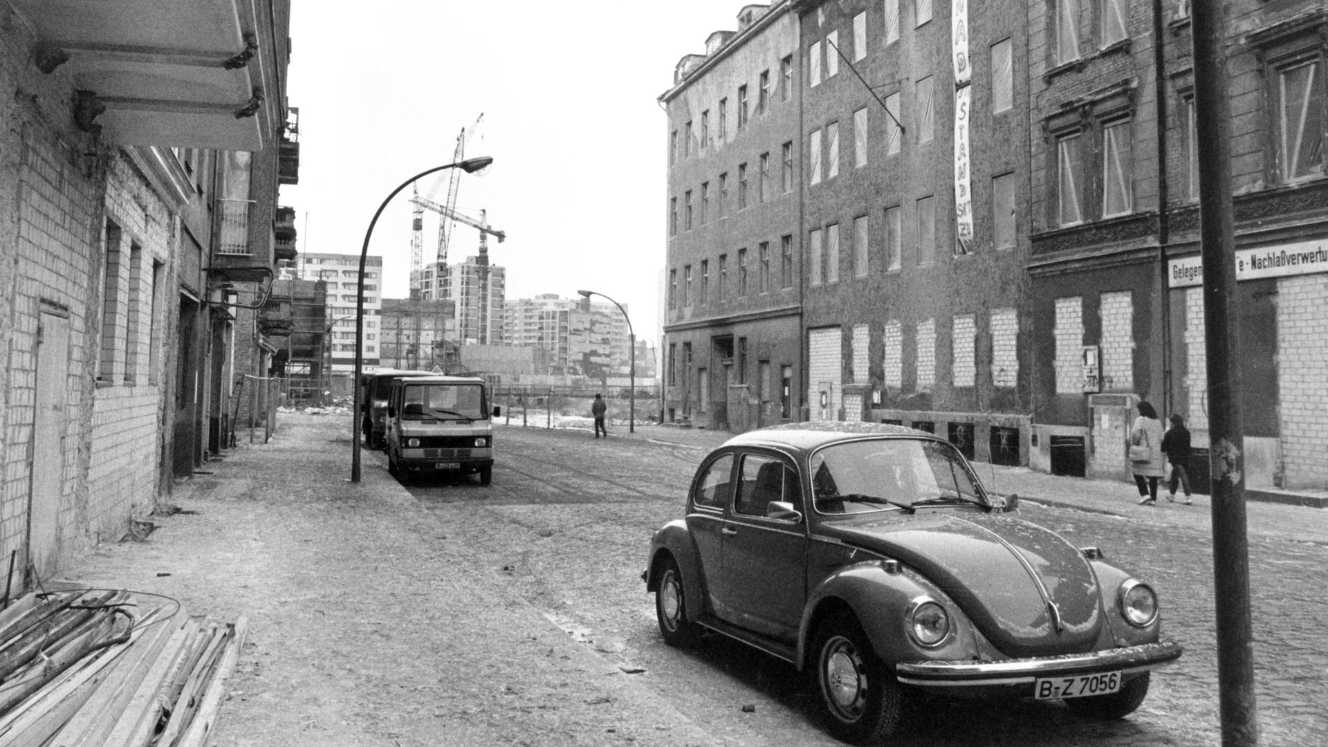 Schwarz-weiß-Aufnahme von einer Straße in Berlin-Kreuzberg Anfang der 1980er-Jahre. Auf der linken Seite werden Altbauten restauriert, auf der rechten stehen Abrisshäuser. Im Vordergrund parkt ein VW Käfer. Schwarz-weiß-Aufnahme von einer Straße in Berlin-Kreuzberg Anfang der 1980er-Jahre. Auf der linken Seite werden Altbauten restauriert, auf der rechten stehen Abrisshäuser. Im Vordergrund parkt ein VW Käfer.