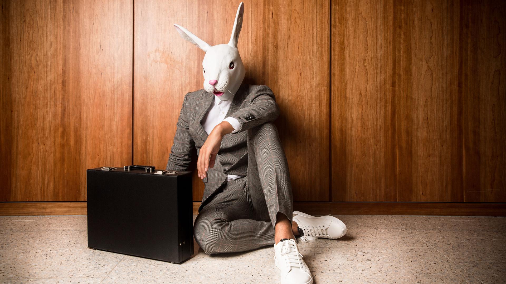 Ein Businessmann im Anzug und Aktenkoffer mit einer weißen Hasenmaske auf dem Kopf. Ein Businessmann im Anzug und Aktenkoffer mit einer weißen Hasenmaske auf dem Kopf.