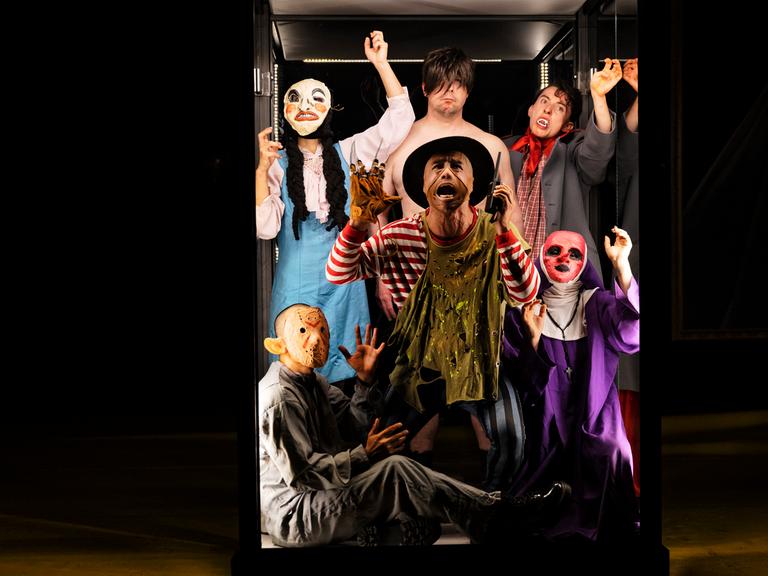 Schauspieler, teilweise mit Masken lehnen ausdrucksstark gegen eine Scheibe
