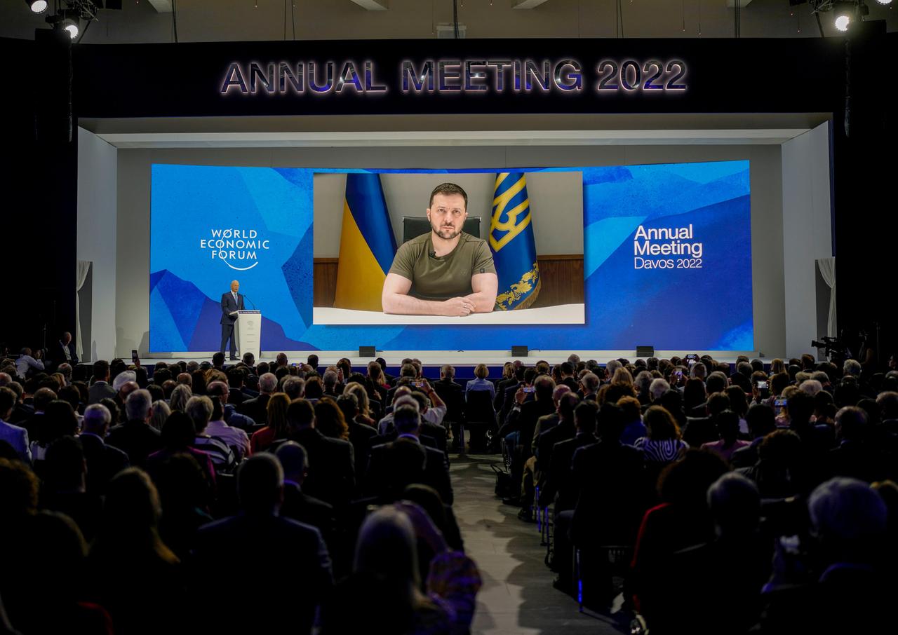 Der ukrainische Präsident Selenskyj auf einer Videoleinwand beim Weltwirtschaftsforum in Davos. Davor sitzen Teilnehmer in zwei Blöcken.