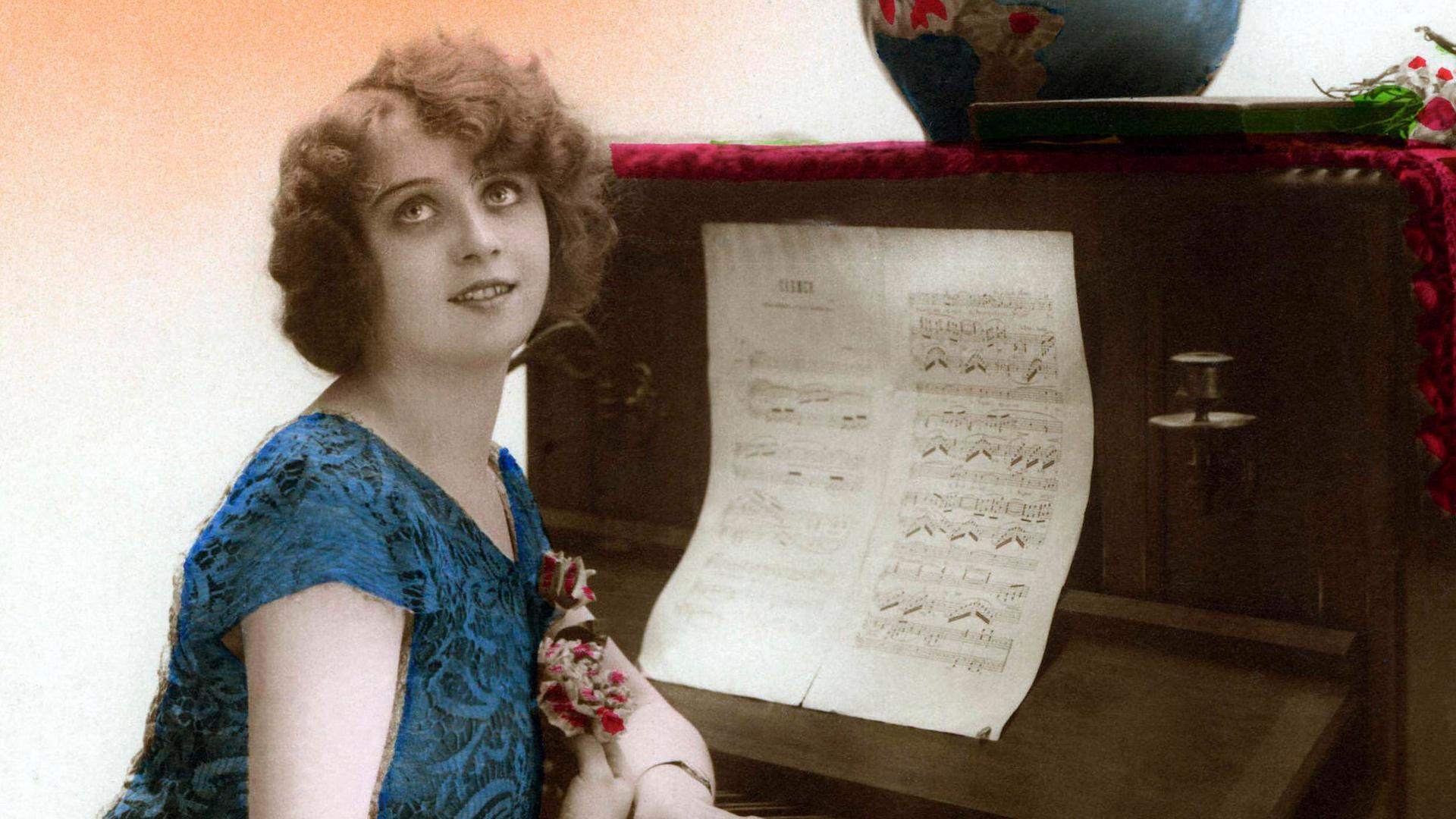 Historische Fotographie um 1905 einer Frau, die am Klavier sitzt und dabei verklärt die Augen nach oben richtet. Historische Fotographie um 1905 einer Frau, die am Klavier sitzt und dabei verklärt die Augen nach oben richtet.
