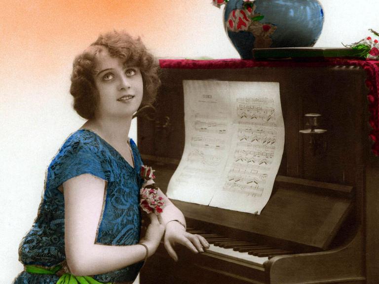 Historische Fotographie um 1905 einer Frau, die am Klavier sitzt und dabei verklärt die Augen nach oben richtet.