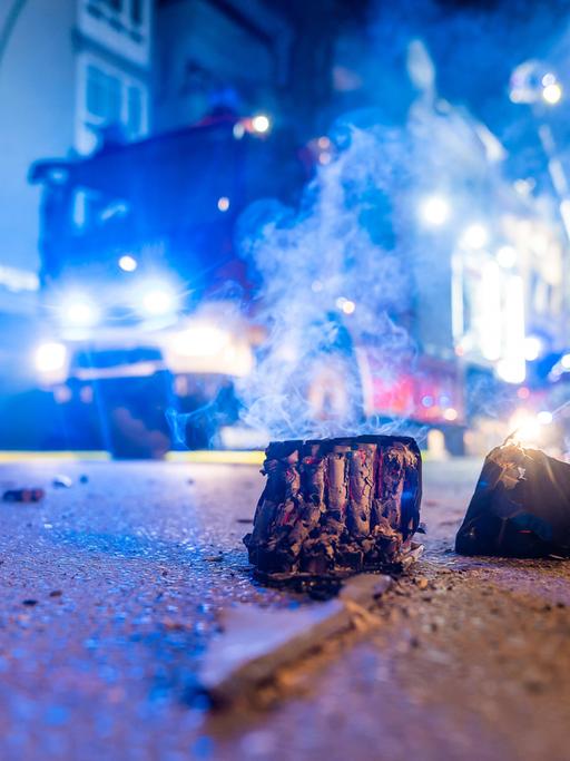Auf einer nächtlichen Straße liegt abgebranntes Feuerwerk, dahinter steht ein Feuerwehrauto.