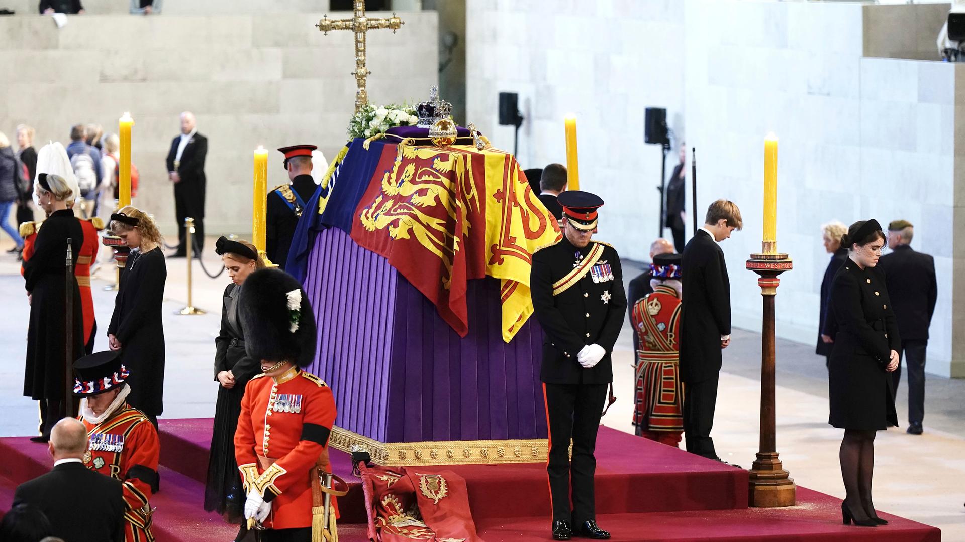 Uniformierte Männer und Frauen in schwarzer Trauerkleidung umstehen auf eine, rotem Podest einen Sarg, der mit einer Flagge, Blumen und einem goldenen Kreuz geschmückt ist. Uniformierte Männer und Frauen in schwarzer Trauerkleidung umstehen auf eine, rotem Podest einen Sarg, der mit einer Flagge, Blumen und einem goldenen Kreuz geschmückt ist.