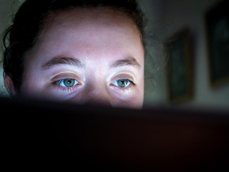 Nahaufnahme einer jungen Frau, die konzentriert auf einen Computerbildschirm schaut. Über dem Monitorrand sind ihre grünen Augen zu sehen.
